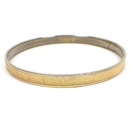 Angled side view of the Mid Century vintage Crown Trifari bangle bracelet. It is two tone in color with matte brushed gold tone color in the middle and a thin silver tone color edge. 