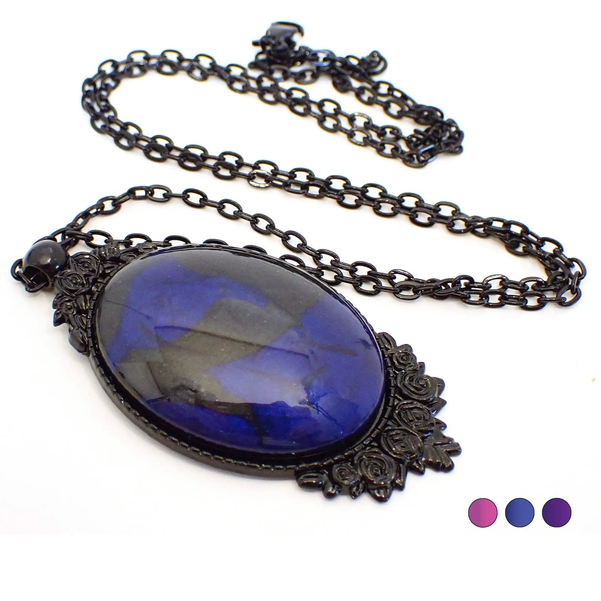 Top view of the handmade Goth Victorian style pendant necklace. The chain and setting are black coated metal. The chain has cable links and a lobster claw clasp at the end. The setting is oval shaped with a rose floral design on the top and bottom. The resin cab in the middle is oval and has pearly black and shades of pearly dark blue resin.