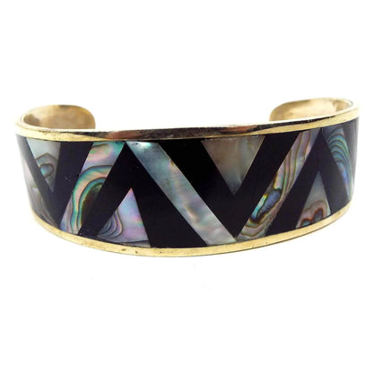 Front view of the retro vintage Mexican chevron cuff bracelet. It is a light gold tone in color with black enameled chevron patter with angled rows of abalone shell in between.
