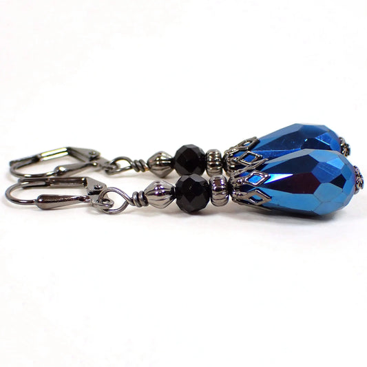 Side view of the handmade teardrop earrings. The metal is gunmetal gray in color. There are black rondelle shaped faceted glass beads at the top. The bottom teardrop beads are bright metallic blue faceted glass.