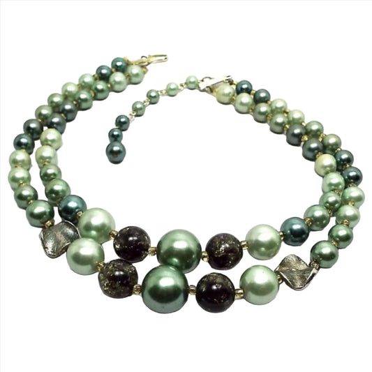Angled view of the Japan Mid Century vintage multi strand beaded necklace. There are two strands of pearly round and round confetti style beads in varying shades of green. There is a gold tone hook clasp at the end..