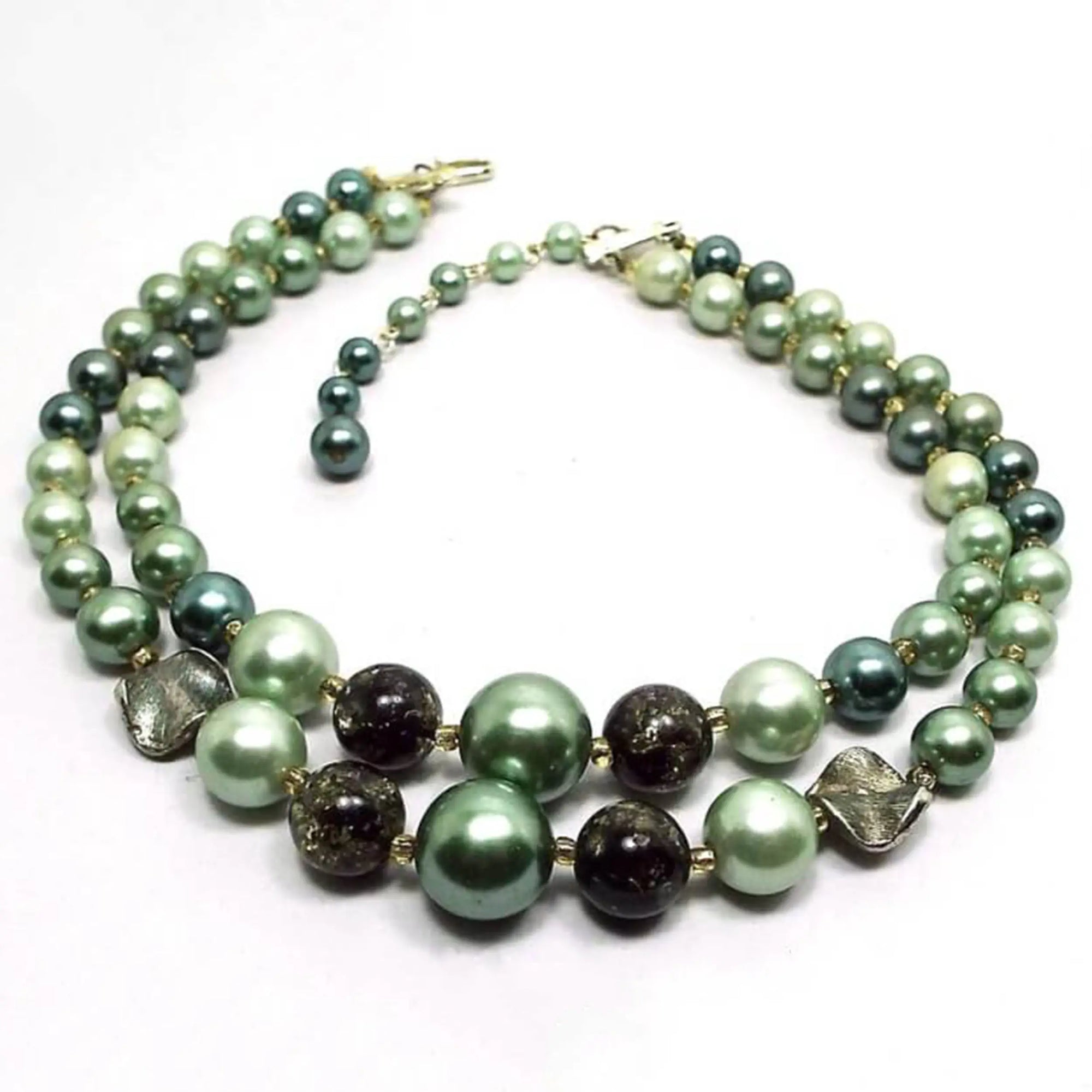 Angled view of the Japan Mid Century vintage multi strand beaded necklace. There are two strands of pearly round and round confetti style beads in varying shades of green. There is a gold tone hook clasp at the end..