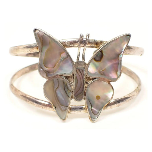 Front view of the retro vintage Alpaca silver butterfly cuff bracelet. The silver tone metal is slightly darkened from age. The butterfly has pieces of inlaid abalone shell that is pearly and has different light colors.