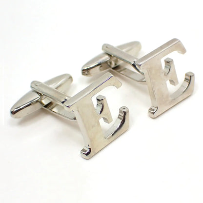 Enlarged angled view of the retro vintage initial cufflinks. They are silver tone in color and shaped like a block letter E.