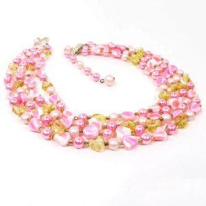 Angled view of the Mid Century Vintage Japanese beaded necklace. There are round and nugget style beads in pink and yellow. The necklace has four strands of beads with a hook clasp at the end.
