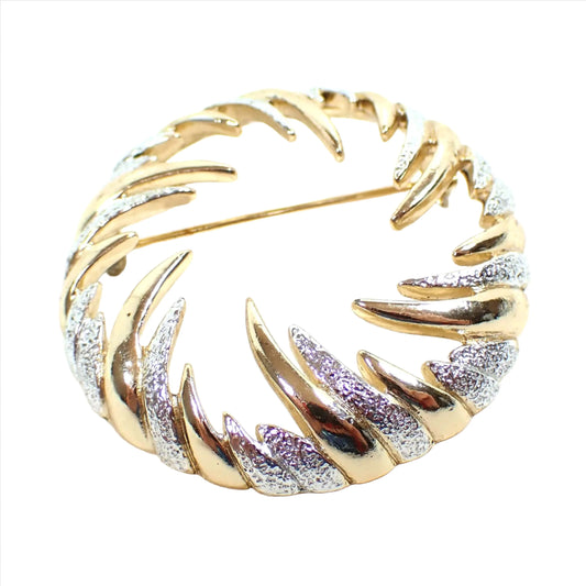 Front view of the retro vintage Sarah Coventry brooch pin. It is round in shape with an open middle. The is a curved spike like design going inward all the way around the brooch. The colors rotate between shiny gold tone plated and textured matte silver tone plated color.