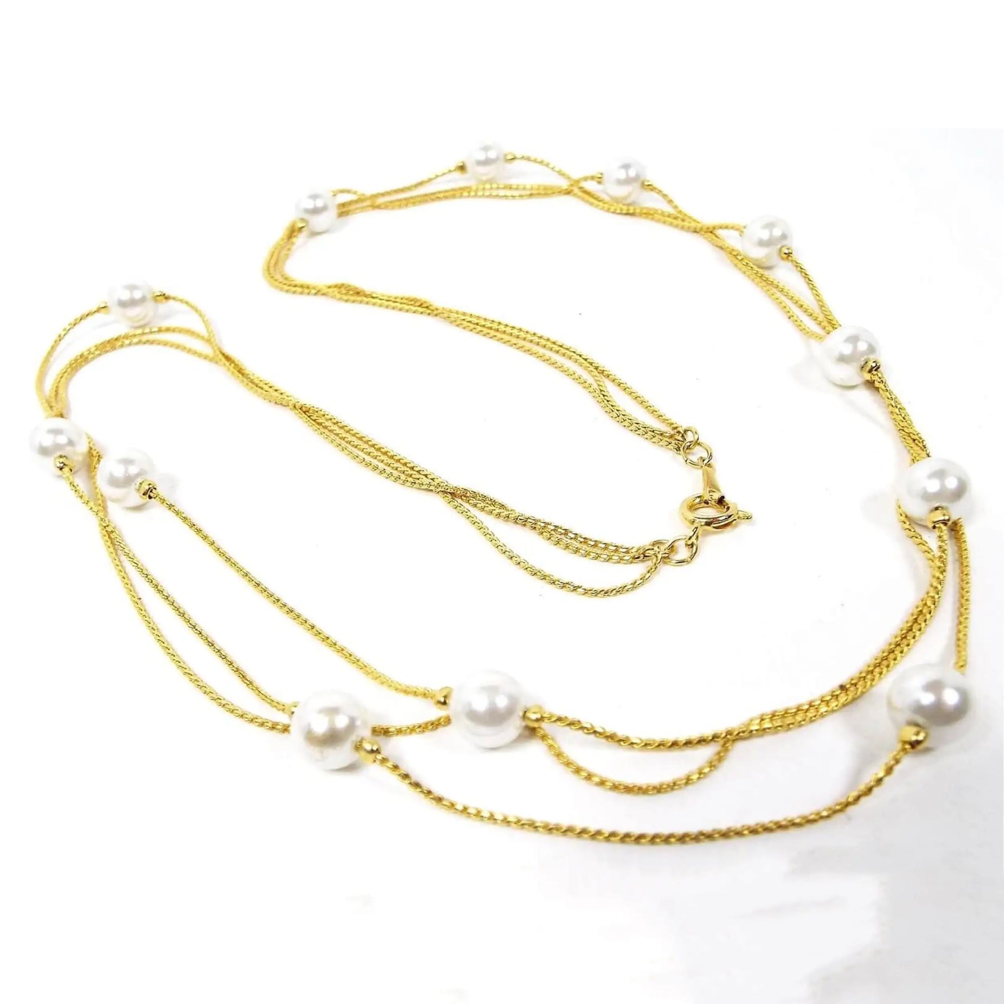 Retro vintage faux pearl beaded chain necklace. It has three thin strands of serpentine chain in gold tone color metal. The imitation pearl beads are scattered here and there throughout the necklace and are pearly white plastic. There is a spring ring clasp at the end.
