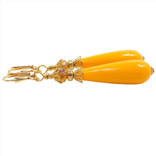 Side view of the handmade yellow teardrop earrings. The metal is gold plated in color. There are long lucite teardrop beads at the bottom in a bright mustard yellow color and faceted glass beads at the top with yellow and orange.