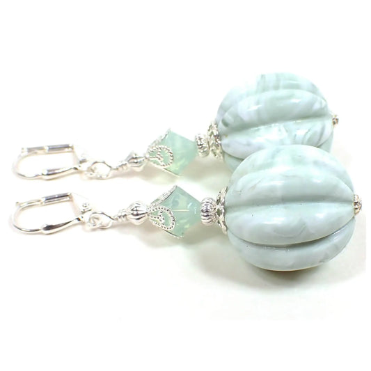 Side view of the handmade earrings with vintage lucite beads. The metal is silver plated in color. There are faceted light mint green glass crystal beads at the top. The bottom beads are large corrugated round shaped and have a marbled light mint green and white design.