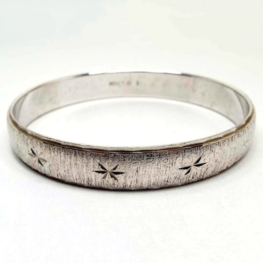 Angled side view of the Mid Century vintage Monet bangle bracelet. It is silver tone in color with textured matte metal all the way around the outside edge. There is a starburst design etched around the bangle as well. The inside is smooth.