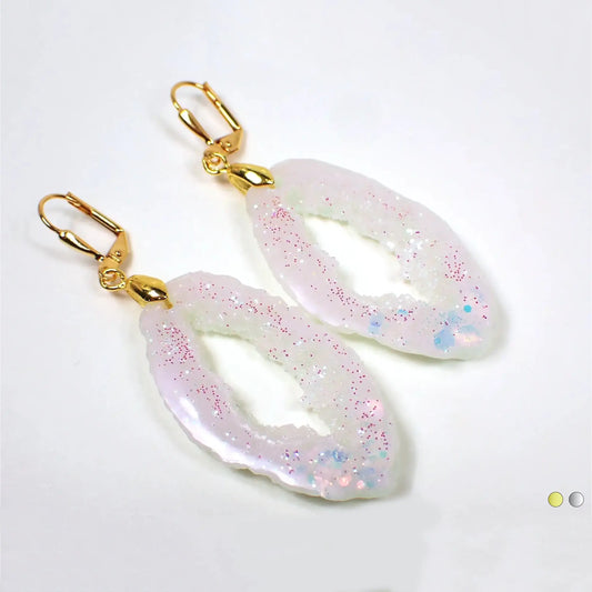 Enlarged angled front view of the gold plated handmade resin druzy geodeo style oval earrings. The resin is an iridescent pearly white color and it has chunky iridescent glitter on one end and tiny iridescent and pink glitter on the other.
