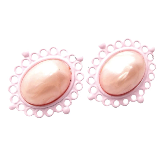 Front view of the Mid Century vintage enameled clip on earrings. They have a filigree oval setting with light pink enamel. There is a plastic cab in the middle with a different shade of light pearly pink.