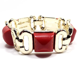 Front view of the retro vintage link bracelet. The metal is gold tone in color. There are red square domed plastic cabs on some links with two open oval metal links in between.