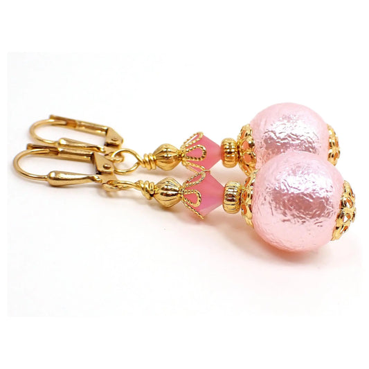Side view of the handmade sphere drop earrings. The metal is gold plated in color. There is a light pink faceted glass crystal at the top. The bottom acrylic bead is round with a bumpy texture and is a light pink in color as well.