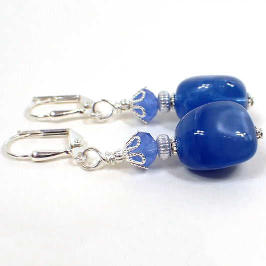 Side view of the handmade drop earrings with vintage lucite beads. The metal is silver plated in color. There are faceted blue glass beads at the top. The bottom vintage lucite beads are nugget shaped and a pearly blue in color.