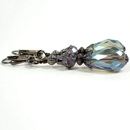 Side view of the handmade teardrop earrings. The metal is gunmetal gray in color. There are rondelle shaped faceted glass beads at the top. The bottom beads are faceted teardrop shaped and both are blue and green in color with an AB coating. The AB coating gives a few flashes of purple and other colors as you move around in the light.