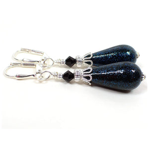 Side view of the handmade earrings with vintage German acrylic glitter beads. The metal is silver plated in color. There are black faceted glass beads at the top. The bottom beads are black acrylic teardrops with teal blue glitter on the outside.