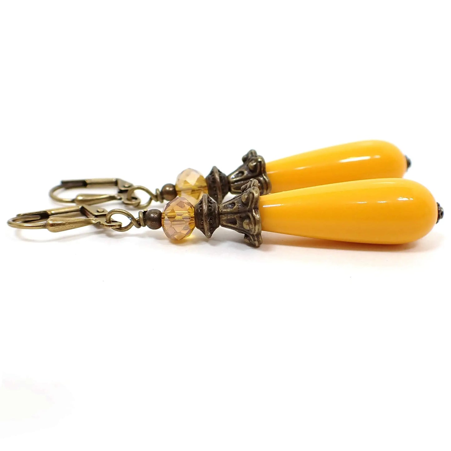 Side view of the handmade yellow teardrop earrings. The metal is antiqued brass in color. There are long lucite teardrop beads at the bottom in a rich yellow color and faceted glass beads at the top with yellow and hints of orange.
