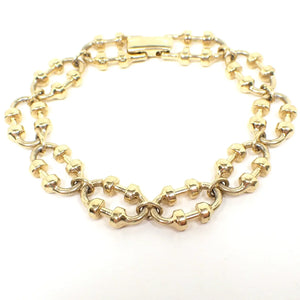 Angled top view of the retro vintage Avon link bracelet. It is gold tone in color and has a snap lock clasp at the end. The links are oval shaped and have rounded areas in the middle with bars in between them. They kind of resemble ovals with a barbell on either side. 
