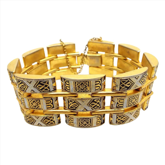 Front view of the Mid Century vintage wide Damascene link bracelet. It has three rows of rectangular links with domed tops. The majority of the metal is gold tone in color. Each link also has a silver tone and black design painted on it.