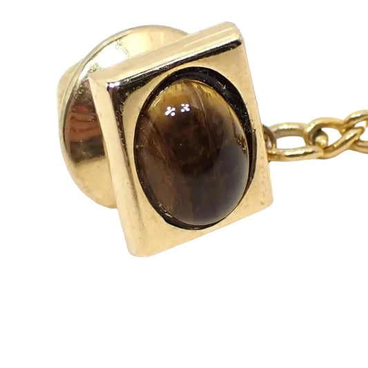 Front view of the Mid Century vintage tiger's eye tie tack. It has a geometric style design with an oval tiger's eye cab and a rectangle setting. The setting is gold tone in color.
