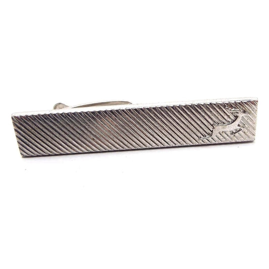 Front view of the Mid Century vintage Hickok tie clip. The metal is silver tone in color. It's shaped like a long rectangle with diagonal lines and a jumping deer or reindeer at the end.
