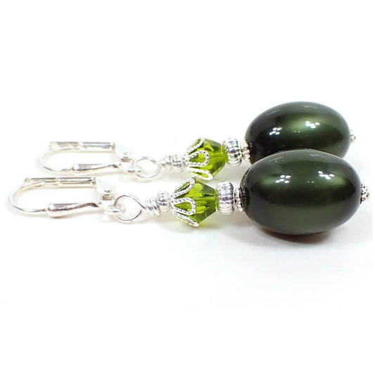 Side view of the handmade earrings with vintage moonglow lucite beads. The metal is silver plated in color. There are green faceted glass crystal beads at the top. The bottom lucite beads are oval shaped and a dark olive green in color. They have an inner like glow as you move around in the light.