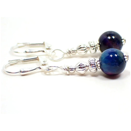 Side view of the small handmade dyed tiger's eye earrings. The metal is silver tone in color. The gemstone beads are round sphere shaped and are dyed blue and have small areas of purple.