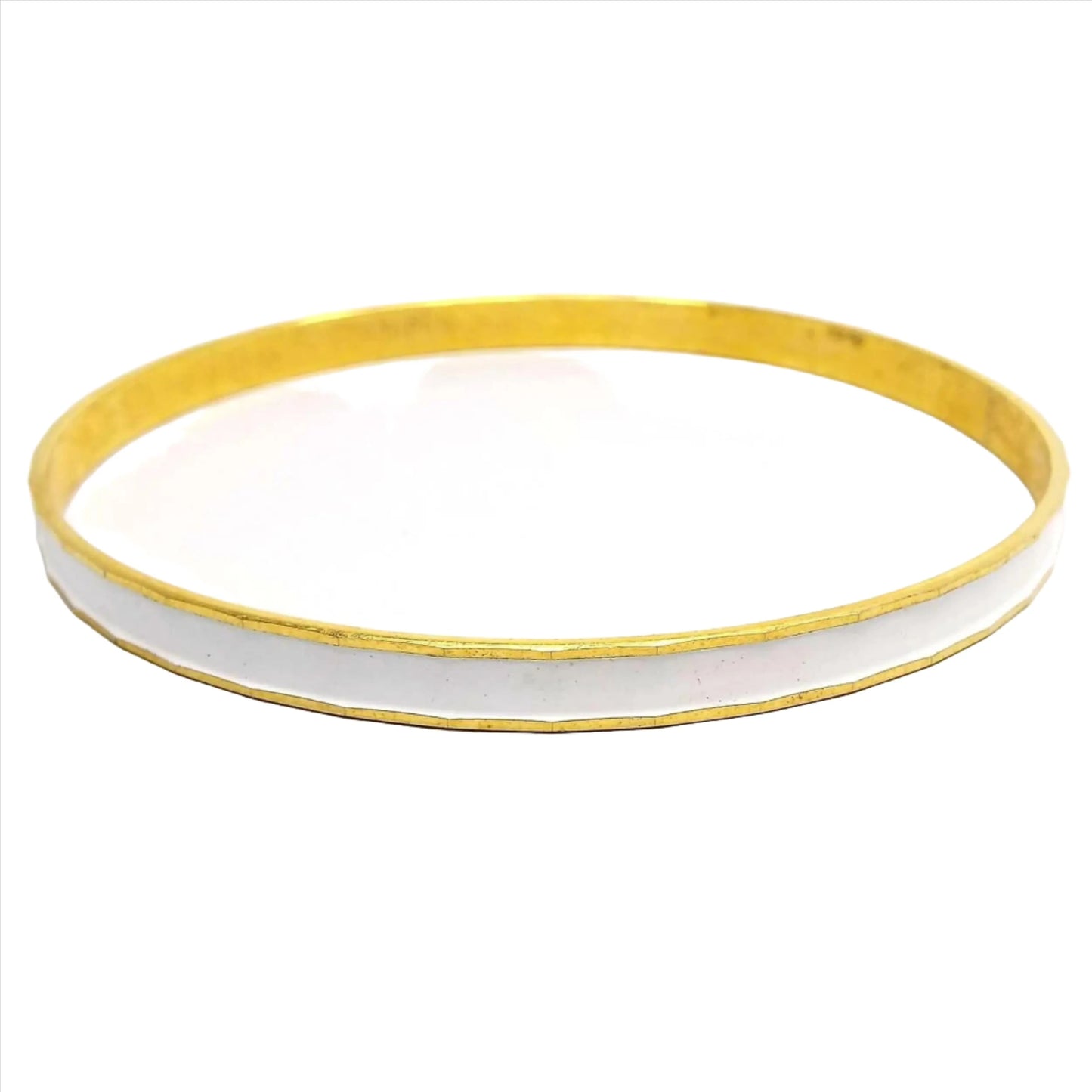 Front view of the Mid Century vintage bangle bracelet from Japan. It is gold tone in color with a faceted edge. The outside edge is enameled white. There are some darkened areas inside the bangle from age.