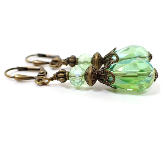 Side view of the vintage style handmade faceted glass crystal teardrop earrings. The metal is antiqued brass in color. The beads are a light AB green. 