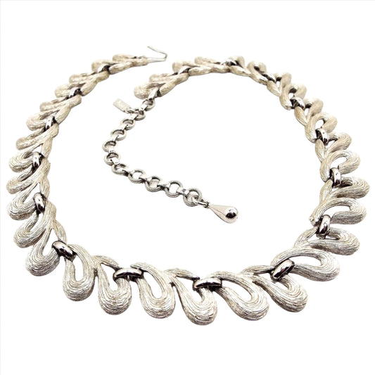 Front view of the retro vintage Monet matte silver tone link necklace. The links are curved teardrop loop design with brushed textured fronts. There is a hook clasp and chain at the end to adjust the size. 
