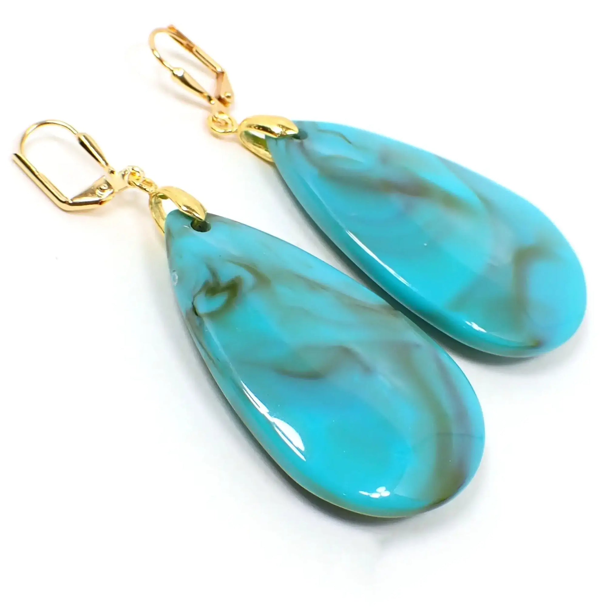 Angled view of the handmade big marbled acrylic teardrop earrings. The metal is gold tone plated in color. They are large puffy teardrop shaped and are mostly turquoise blue color with shades of brown swirled in.