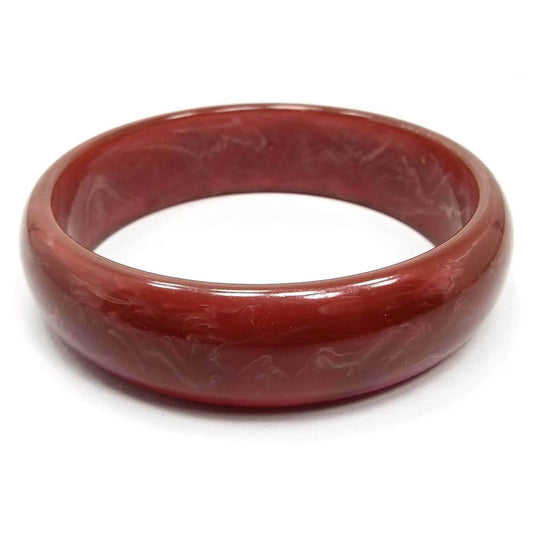 Angled side view of the Mid Century vintage lucite bangle bracelet. It is marbled multi color with shades of red, brown, white, and pink.