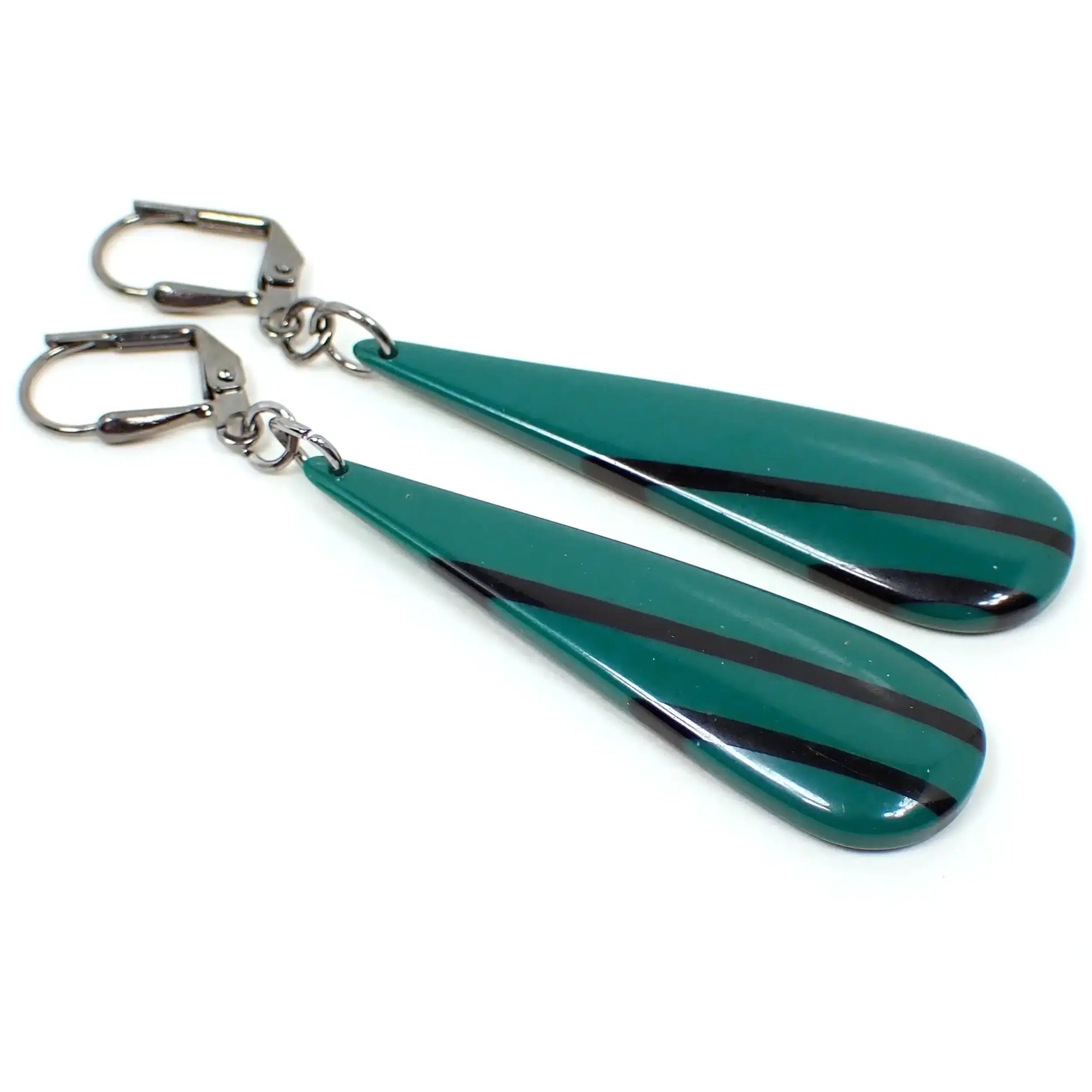 Angled enlarged view of the handmade drop earrings made with vintage resin beads. The metal is gunmetal gray in color. There are long thinner style teardrop beads that are slightly domed on the front. They are a darker green in color with black diagonal stripes.