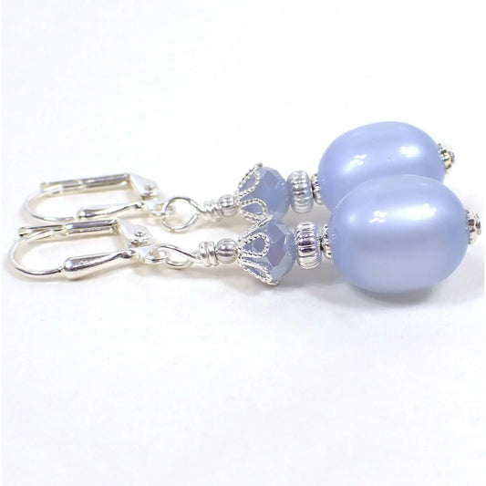 Side view of the handmade drop earrings made with vintage moonglow lucite beads. The metal is silver plated in color. There are faceted light periwinkle blue glass beads at the top. The bottom lucite beads are oval shaped and a light periwinkle blue in color as well. Moonglow lucite has an inner glow type effect as you move around in the light.
