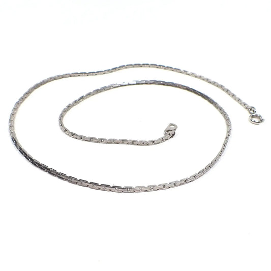 Angled view of the retro vintage South Korean chain necklace. It is silver tone in color and has flat bar shaped links. There is a spring ring clasp and tab at the ends of the chain.