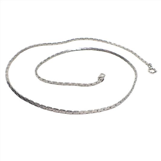 Angled view of the retro vintage South Korean chain necklace. It is silver tone in color and has flat bar shaped links. There is a spring ring clasp and tab at the ends of the chain.