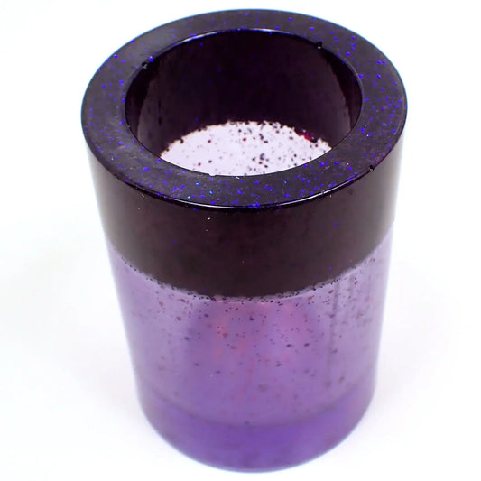 Angled view of the handmade resin makeup brush or toothbrush holder. Nice basic round design with dark pearly purple on top with tiny flecks of blue glitter and semi transparent pearly purple resin on the bottom with iridescent chunky glitter here and there. 