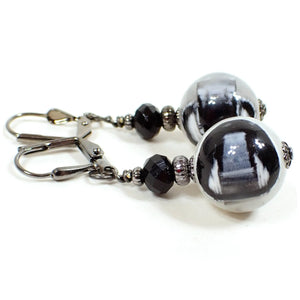 Side view of the handmade drop earrings with vintage lucite beads. The metal is gunmetal gray in color. There are new faceted glass black beads at the top. The bottom lucite beads are primarily white with a black pattern embedded in them. Each lucite bead has a slightly different pattern than the other for a unique appearance.