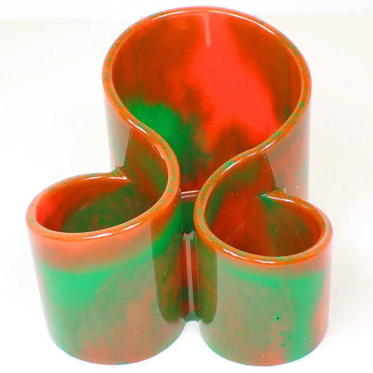 Front view of the handmade resin neon makeup brush  holder. It has a curvy style with three rounded open area to put makeup brushes or other small items. The color is marbled with large areas of neon orange and green.