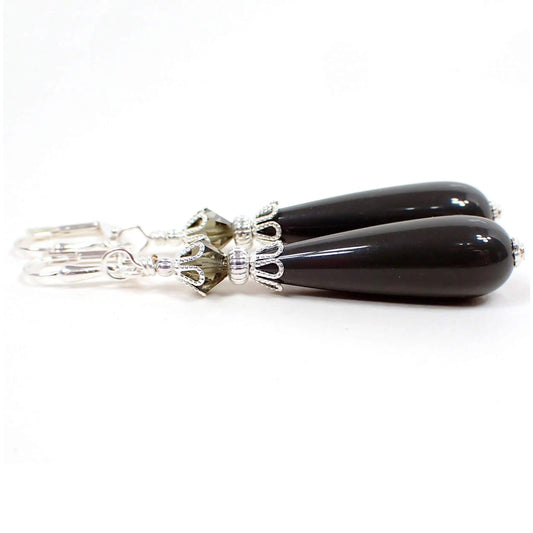 Side view of the handmade teardrop earrings made with vintage lucite beads. The metal is silver plated in color. There are gray faceted glass crystal beads at the top. The bottom lucite beads are teardrop shaped and a dark gray in color.