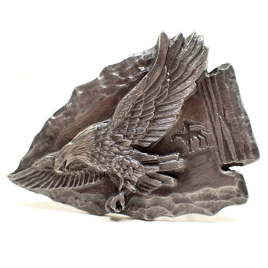 Enlarged front view of the retro vintage Siskiyou belt buckle. It's pewter gray and shaped like an arrowhead. There is a flying eagle on the front area and a small Native American riding a horse in the background.