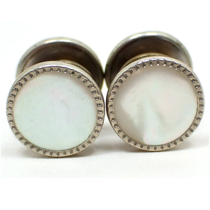 Enlarged view of one side of the Art Deco 1920's Snap link cufflinks. The metal is silver tone in color. They are round with an indented design all the way around the edge. They each have two sides and a middle area that snaps together in the middle that can be partially seen in the photo. The middle of each side has a mother of pearl shell cab that is pearly white in color.
