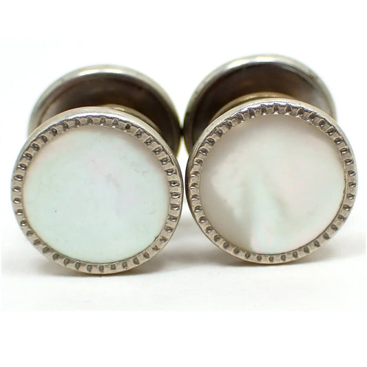 Enlarged view of one side of the Art Deco 1920's Snap link cufflinks. The metal is silver tone in color. They are round with an indented design all the way around the edge. They each have two sides and a middle area that snaps together in the middle that can be partially seen in the photo. The middle of each side has a mother of pearl shell cab that is pearly white in color.