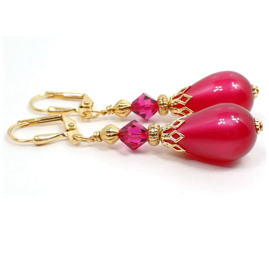 Side view of the handmade teardrop earrings with vintage moonglow lucite beads. The metal is gold plated in color. There is a new faceted glass crystal bicone bead at the top. The bottom bead is teardrop shape and has an inside glowy effect as you move around. Both beads are a bright pink in color.