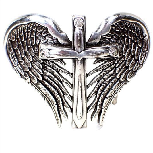 Front view of the pre owned Nocona belt buckle. It is detailed and shaped like a set of angel wings with a cross in the middle of it. The cross has a rhinestone at each cross end at the top. The metal is antiqued silver tone plated in color. 