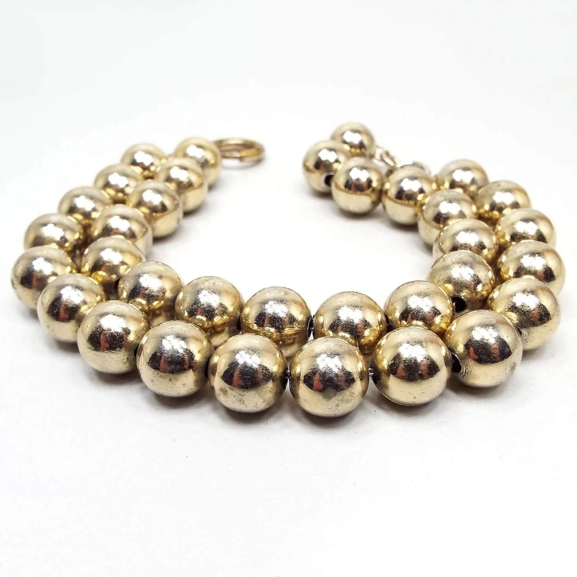 Angled view of the Mid Century vintage metal beaded bracelet. There are two strands of gold tone metal ball beads strung on thin wire. The end has a spring ring clasp.