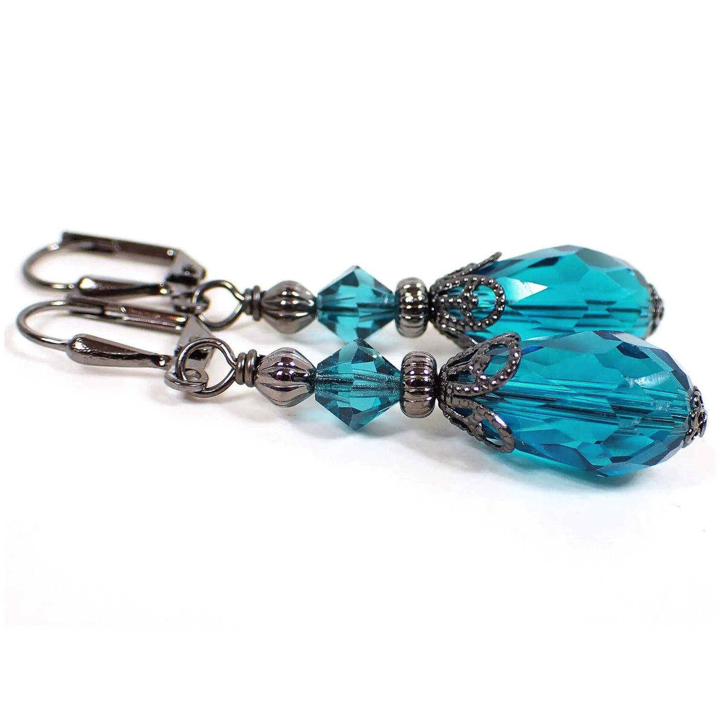 Side view of the handmade teardrop earrings. The metal is gunmetal dark gray in color. There are faceted glass crystal rondelle beads at the top and faceted glass crystal teardrop beads at the bottom. The beads are teal blue in color.