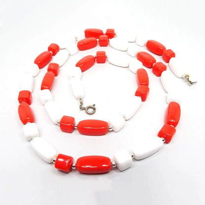 Top view of the retro vintage beaded necklace. There are alternating beads in cute, barrel, and rectangle shape in white and bright red. There is a silver tone spring ring clasp at the end.