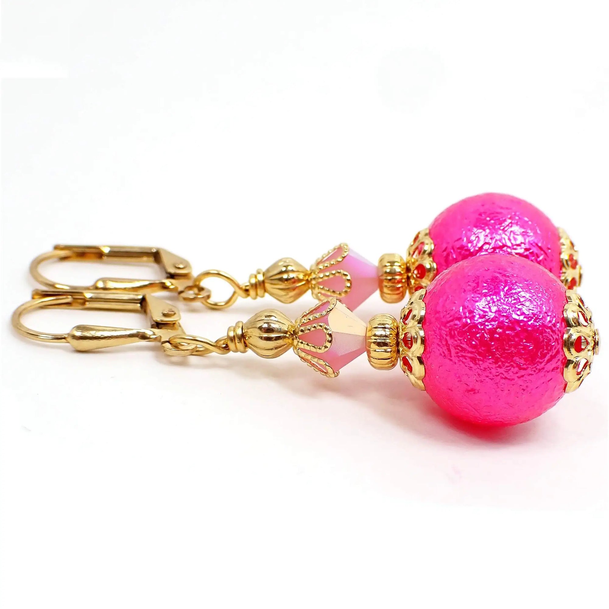 Side view of the handmade sphere drop earrings. The metal is gold plated in color. There is a light pink faceted glass crystal at the top. The bottom acrylic bead is round with a bumpy texture and is bright hot pink in color.